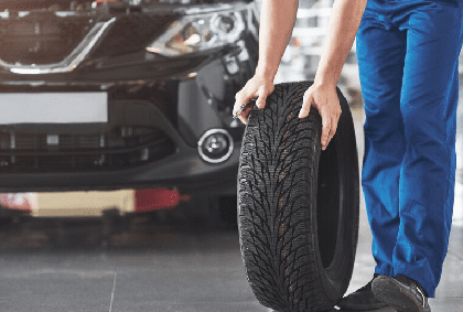 Technician with a blue workwear, holding a wrench and a tire while showing thumb up.