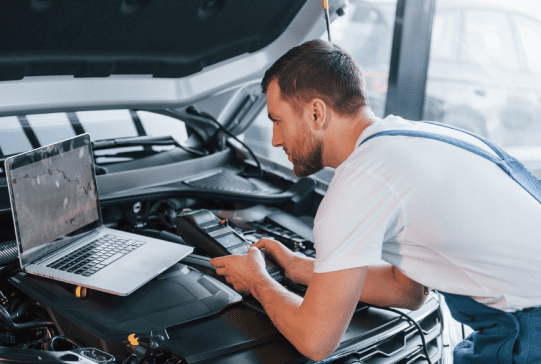 Young man in white shirt and blue uniform repairs automobile