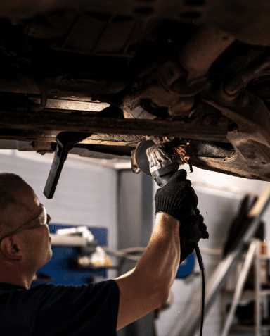 mechanic repairing car suspension with cutting tool at shallow depth of field