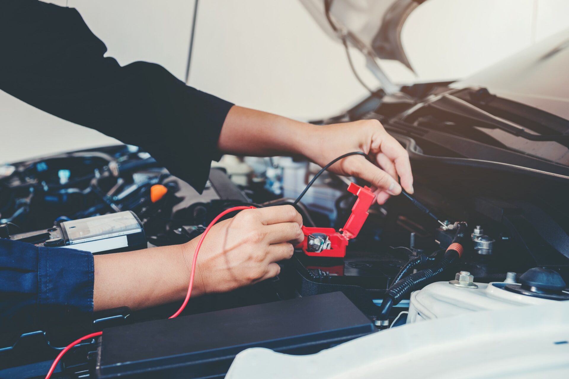 Auto mechanic working with a digital multimeter in a car repair shop.