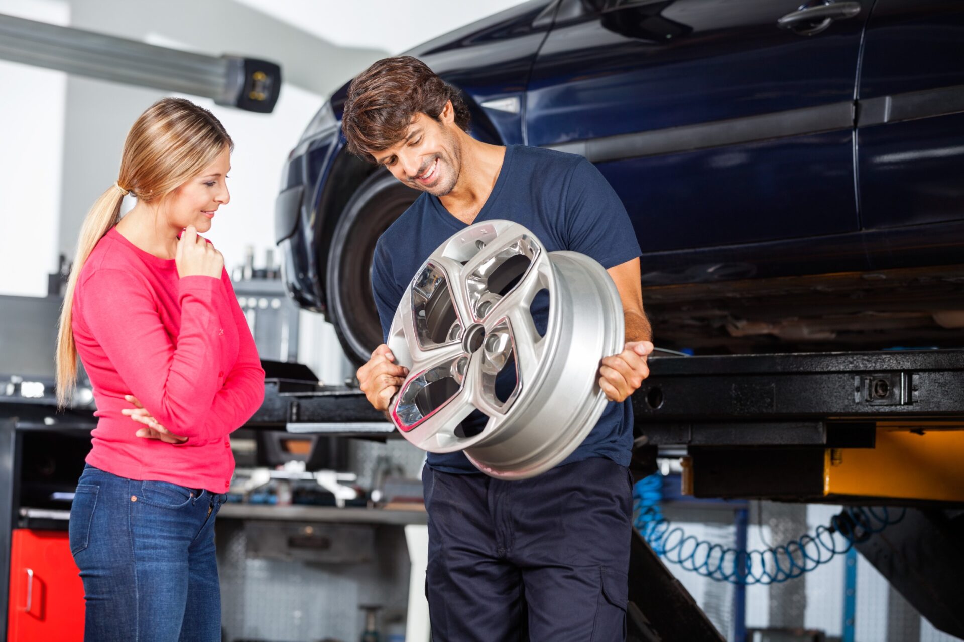 Car mechanic showing a wheel to a female customer in a car service